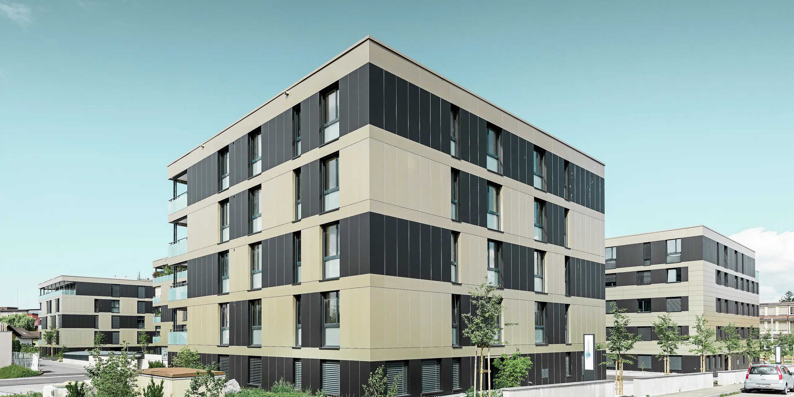 Kockast stanovanjski kompleks z aluminijasto fasado v bronasti barvi in črno-zelenimi elementi