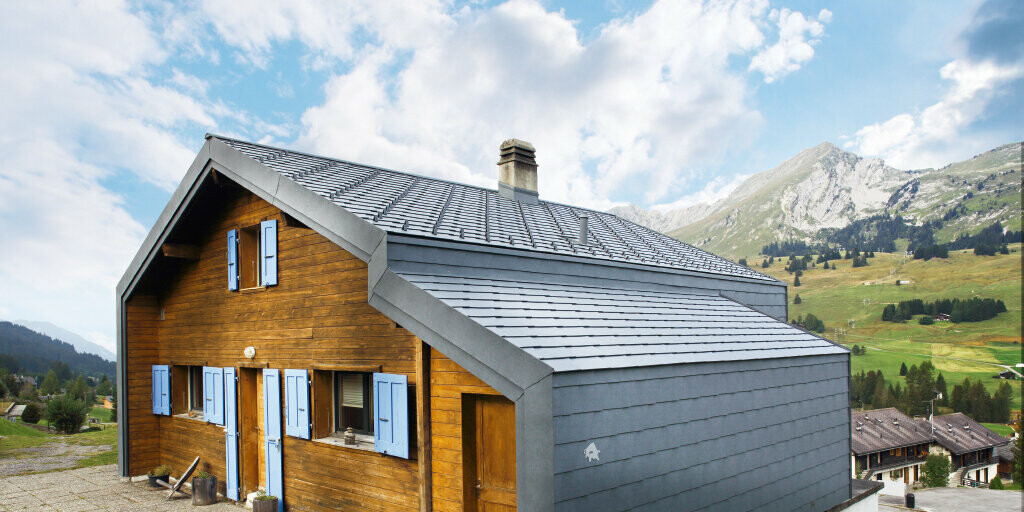 Gorska hiša v Švici z leseno fasado v kombinaciji s strešnim in fasadnim rombom PREFA v kamnito sivi barvi