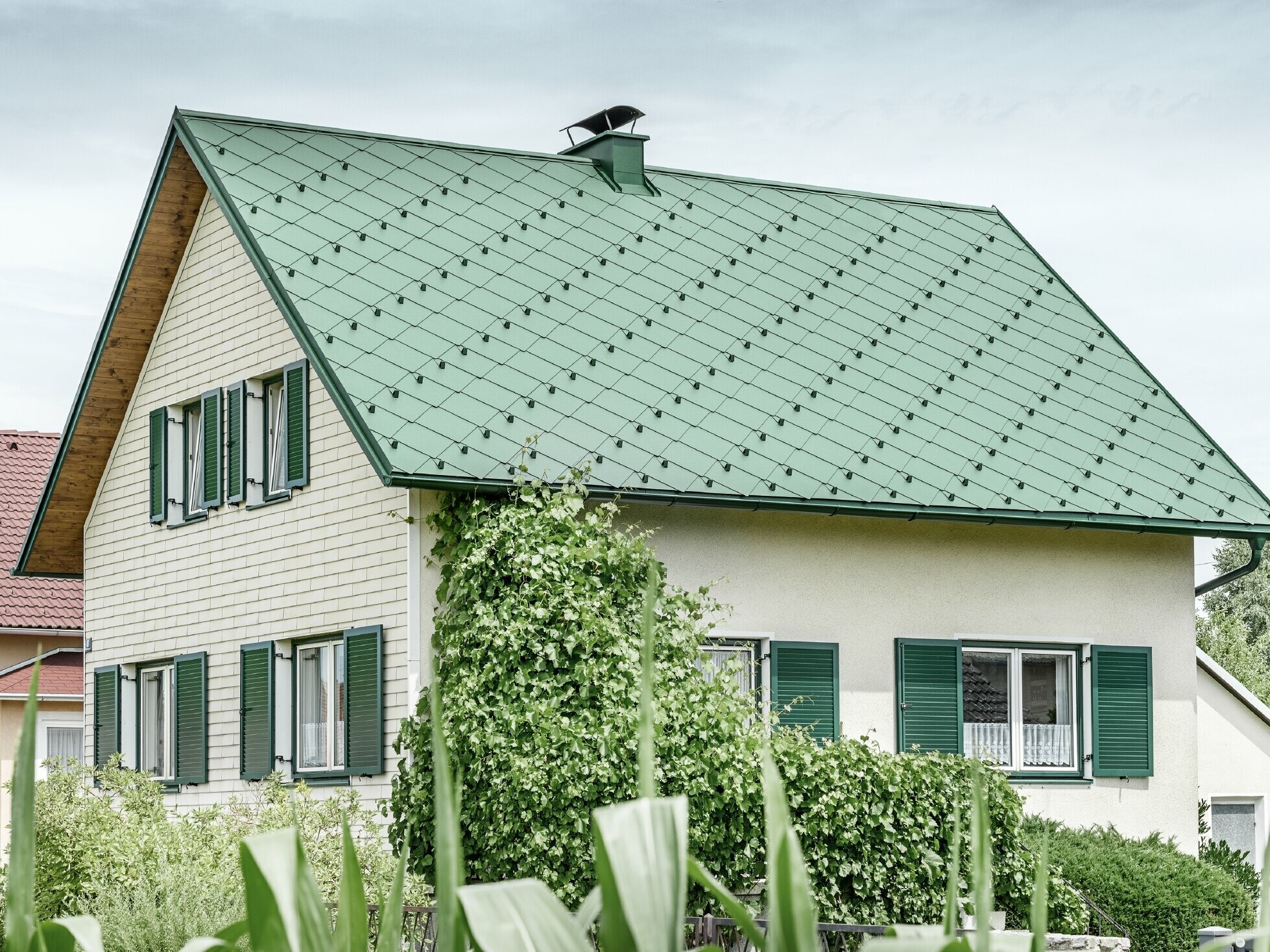 Klasična enodružinska hiša z dvokapno streho s strešno kritino iz aluminija PREFA v mahovo zeleni barvi z zelenimi polkni