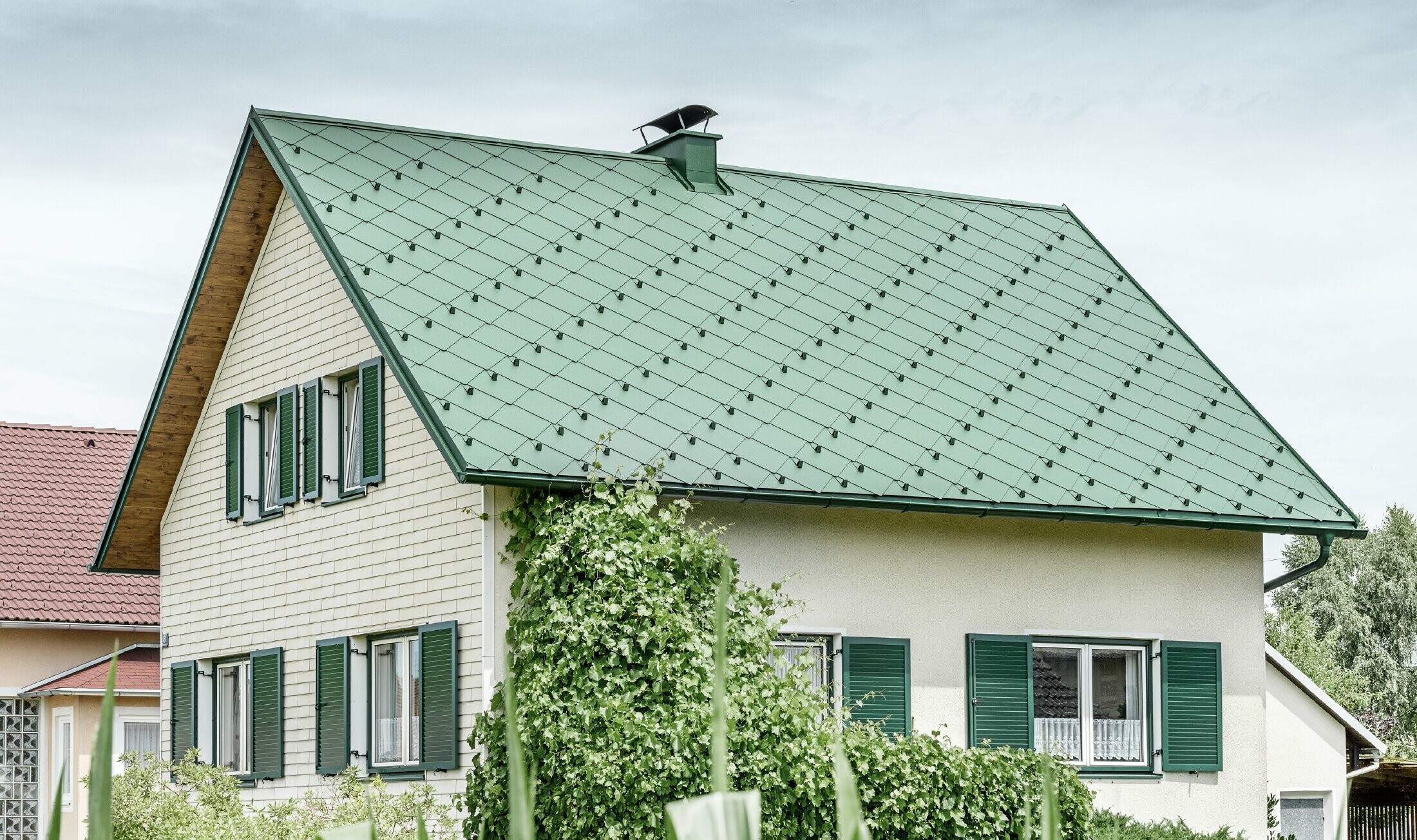 Klasična enodružinska hiša z dvokapno streho s strešno kritino iz aluminija PREFA v mahovo zeleni barvi z zelenimi polkni