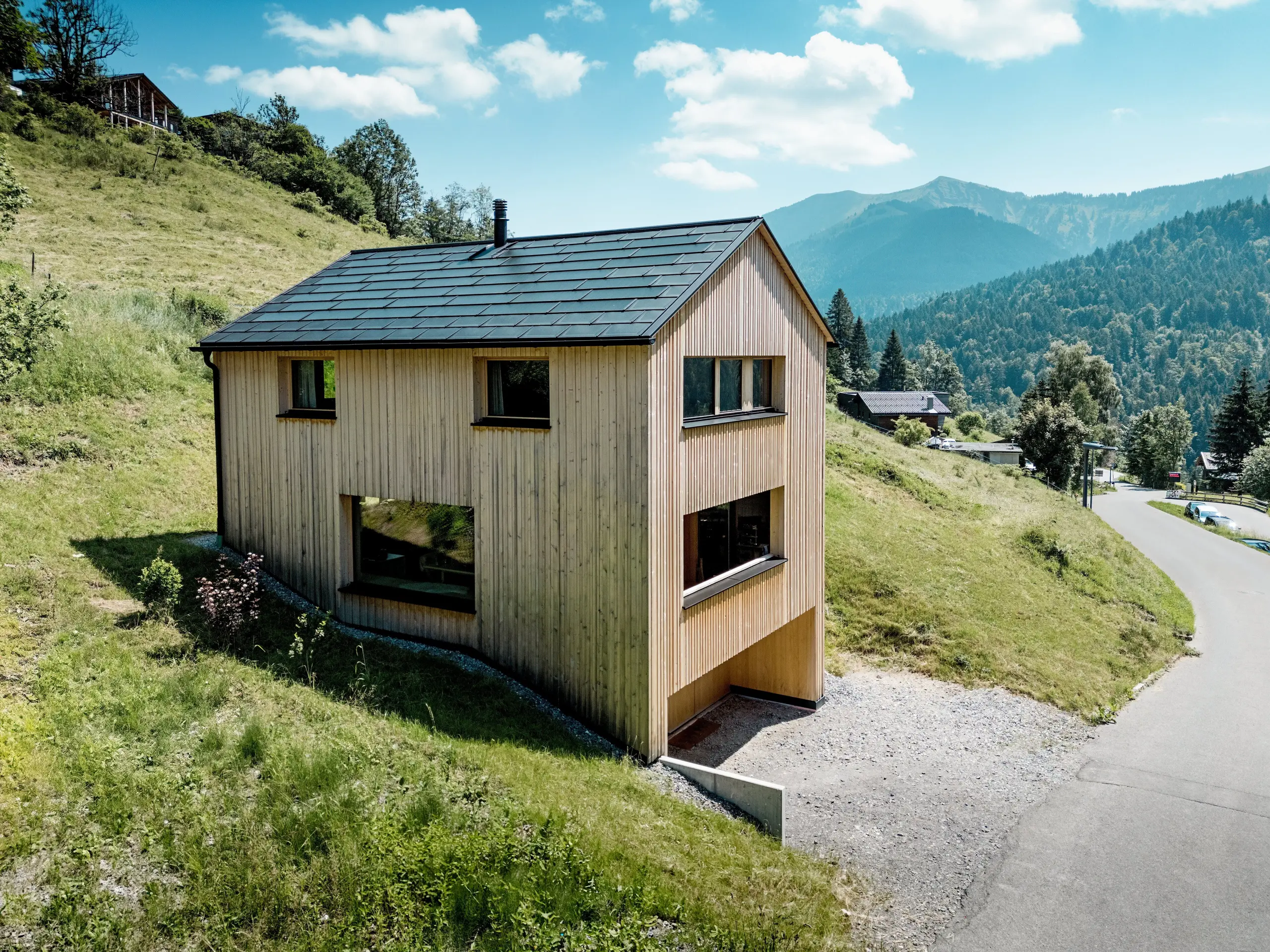 Visoko nad dolino stoji hiša Immi kot jasen leseni monolit na sončnem gorskem pobočju v Ebnitu. Preprosta fasada iz bele smreke in črna solarna streha PREFA ustvarjata močan kontrast s prostrano alpsko pokrajino. Vgrajene solarne strešne plošče in strešne plošče R.16 v črni barvi P.10 zagotavljajo sončno energijo, so odporne proti alpskim vremenskim razmeram in zagotavljajo trajno, harmonično podobo strehe.