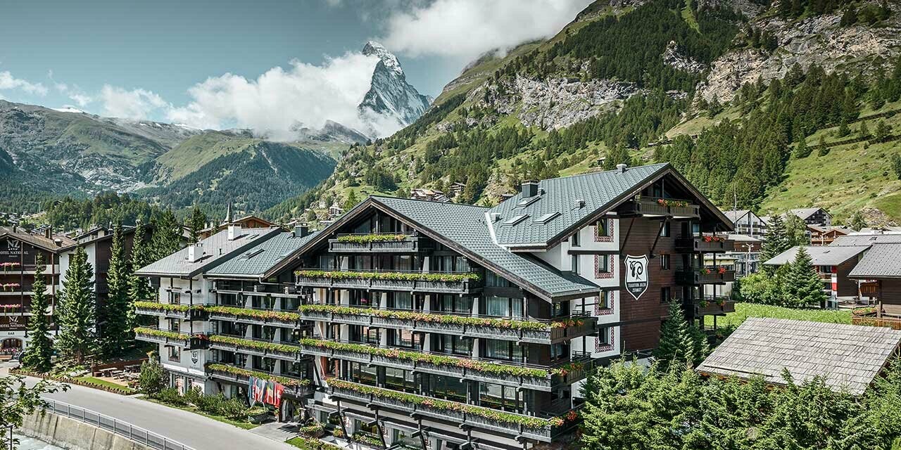 Hotel Alpenhof v Zermattu z Matterhornom v ozadju, z balkoni, temno leseno fasado in aluminijasto streho PREFA v antracitni barvi