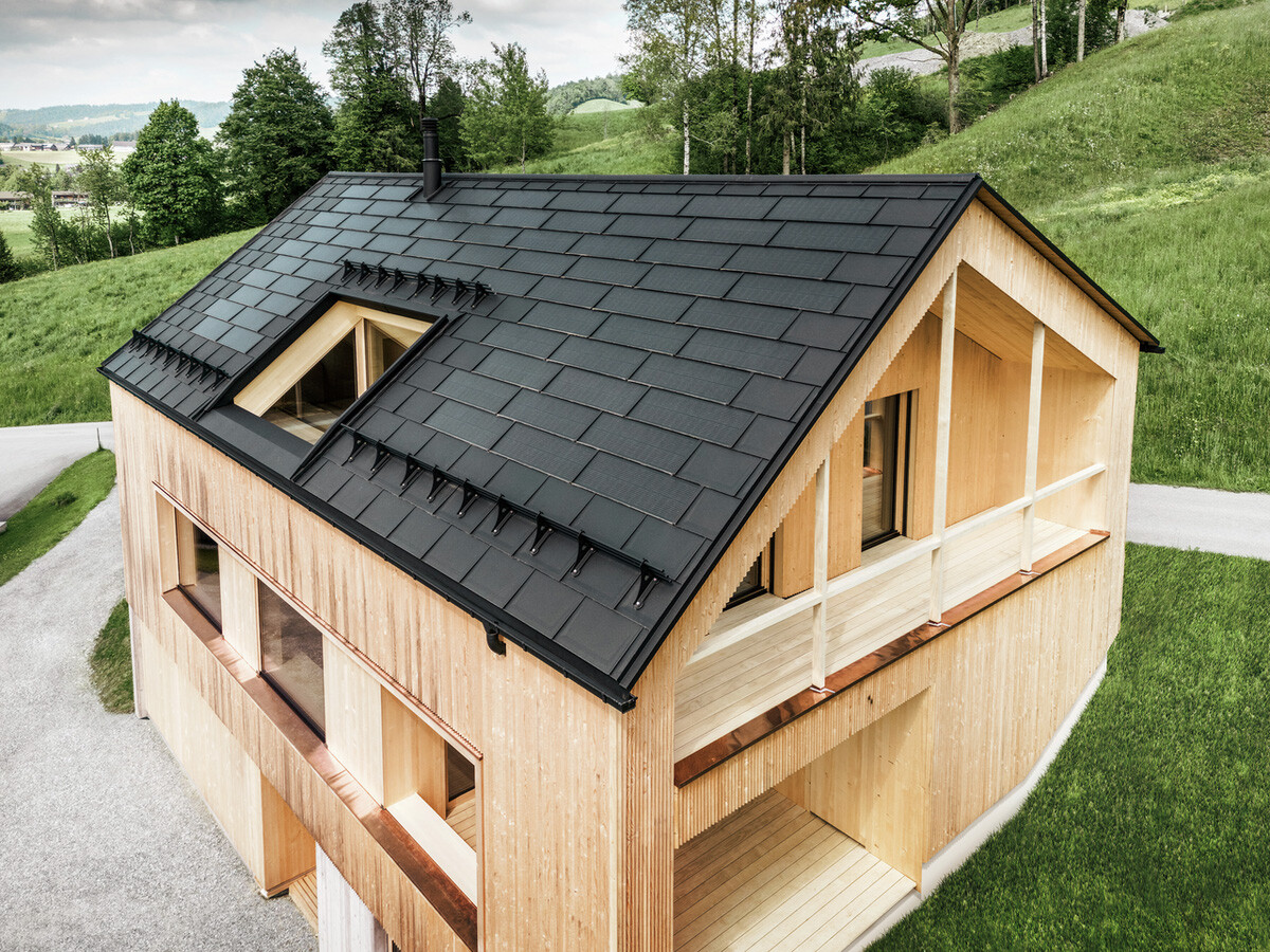 Enodružinska hiša v avstrijskem kraju Egg s solarno strešno ploščo PREFA in strešno ploščo R.16 PREFA v črni barvi v kombinaciji z leseno fasado.