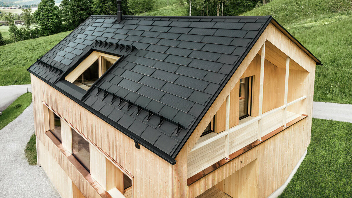 Enodružinska hiša v avstrijskem kraju Egg s solarno strešno ploščo PREFA in strešno ploščo R.16 PREFA v črni barvi v kombinaciji z leseno fasado.