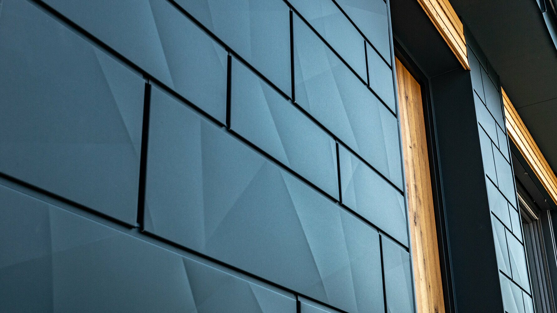 PREFA fasadni paneli v prepognjenem videzu; Aluminijasti elementi PREFA Siding.X v antracitni, kombinirani z leseno fasado.