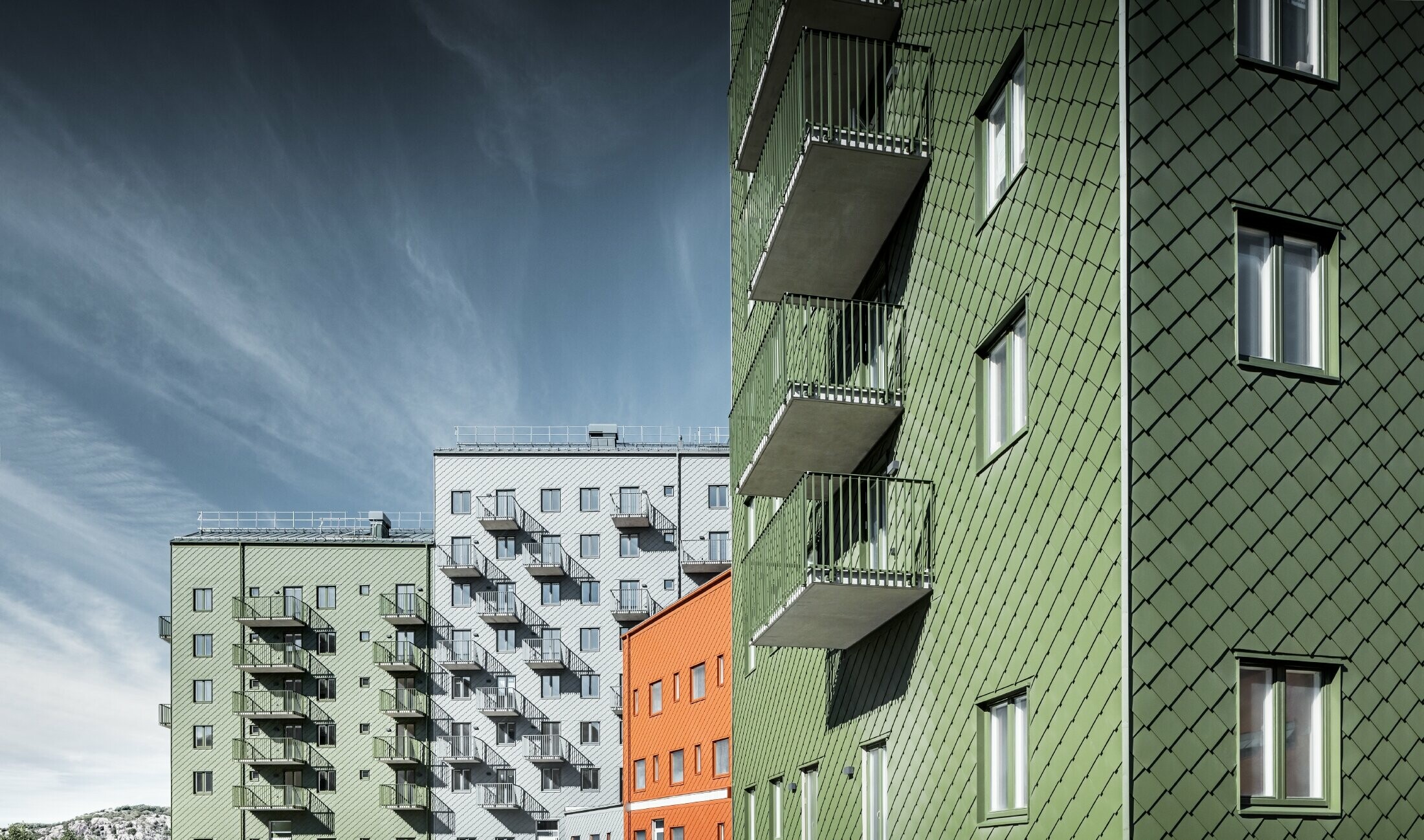 Mehrere Wohnhäuser nebeneinander, eingekleidet mit der PREFA Wandraute 29 × 29 in den Farben Ziegelrot, Olivgrün und Hellgrau.