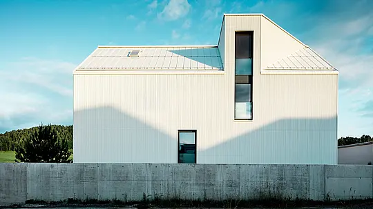 Sodobna enodružinska hiša v Freistadtu je bila fotografirana iz stranskega zornega kota, da bi poudarili izrazit dizajn fasade in strehe. Bela PREFALZ-aluminijasta obloga v kombinaciji s strmim dvokapnim strešnim naklonom in ozkimi okni daje stavbi sodoben in brezčasen videz. Vertikalni žlebički fasade stavbi dajejo dinamičen, teksturiran videz. Igra svetlobe, ki pada na fasado, ustvarja zanimive senčne učinke in poudarja natančne linije oblikovanja. To jasno in minimalistično arhitekturo poudarja trajna in vremensko odporna fasada PREFALZ, ki je znana po svoji trajnosti in enostavnem vzdrževanju.