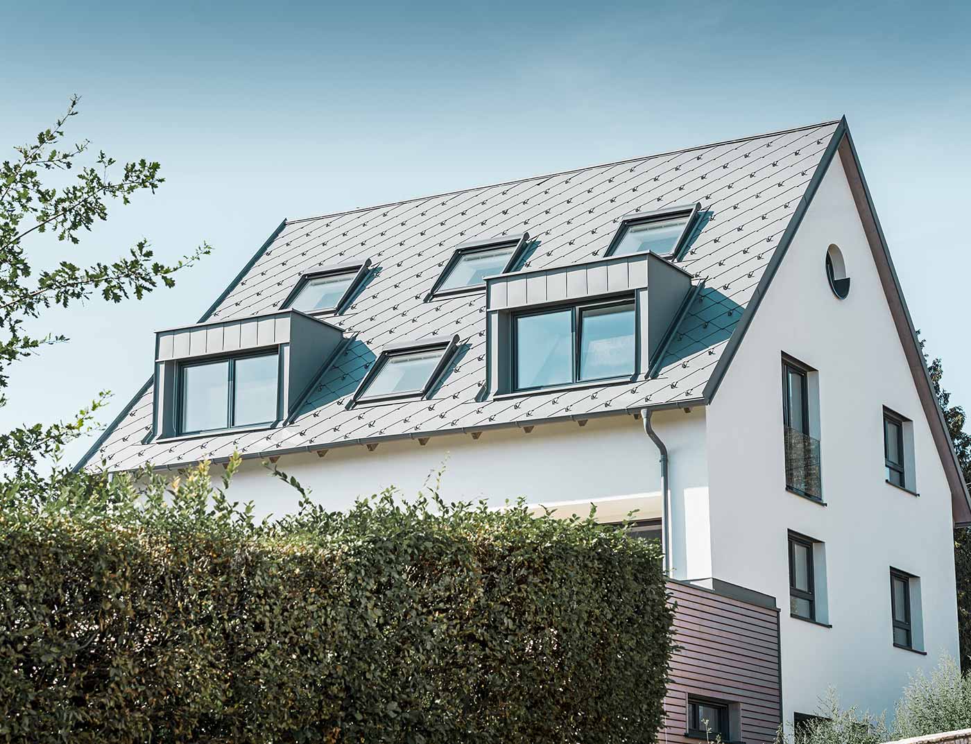 PREFA Dachraute 44 × 44 Hellgrau Referenz Klassisches Satteldach mit zwei Gauben und mehreren Dachfenstern, eingedeckt mit der PREFA Dachraute 44 × 44 in Hellgrau.